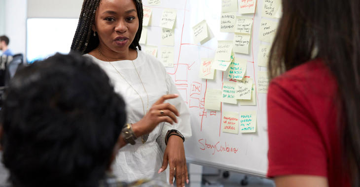 Woman talking at whiteboard post it notes 